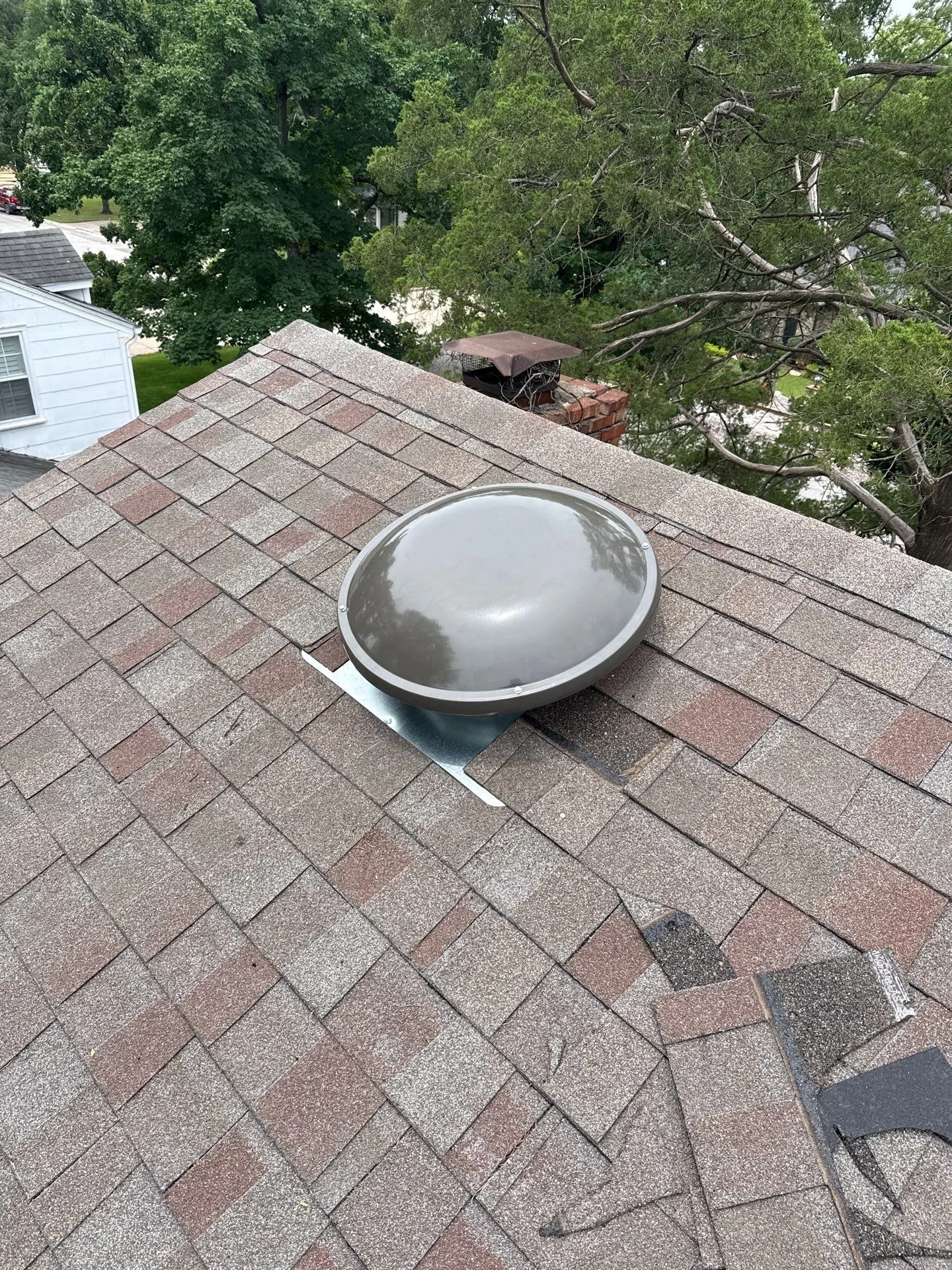Domed skylight installed on asphalt shingle roof with metal frame and trim