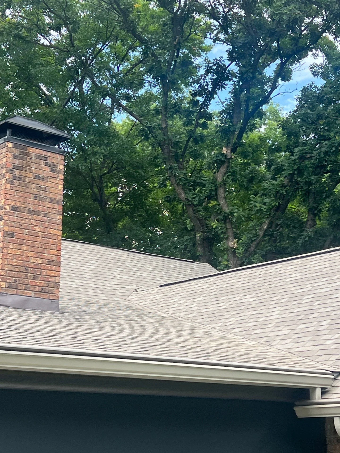 Light gray architectural shingles on multi-plane roof with brick chimney and metal flashing