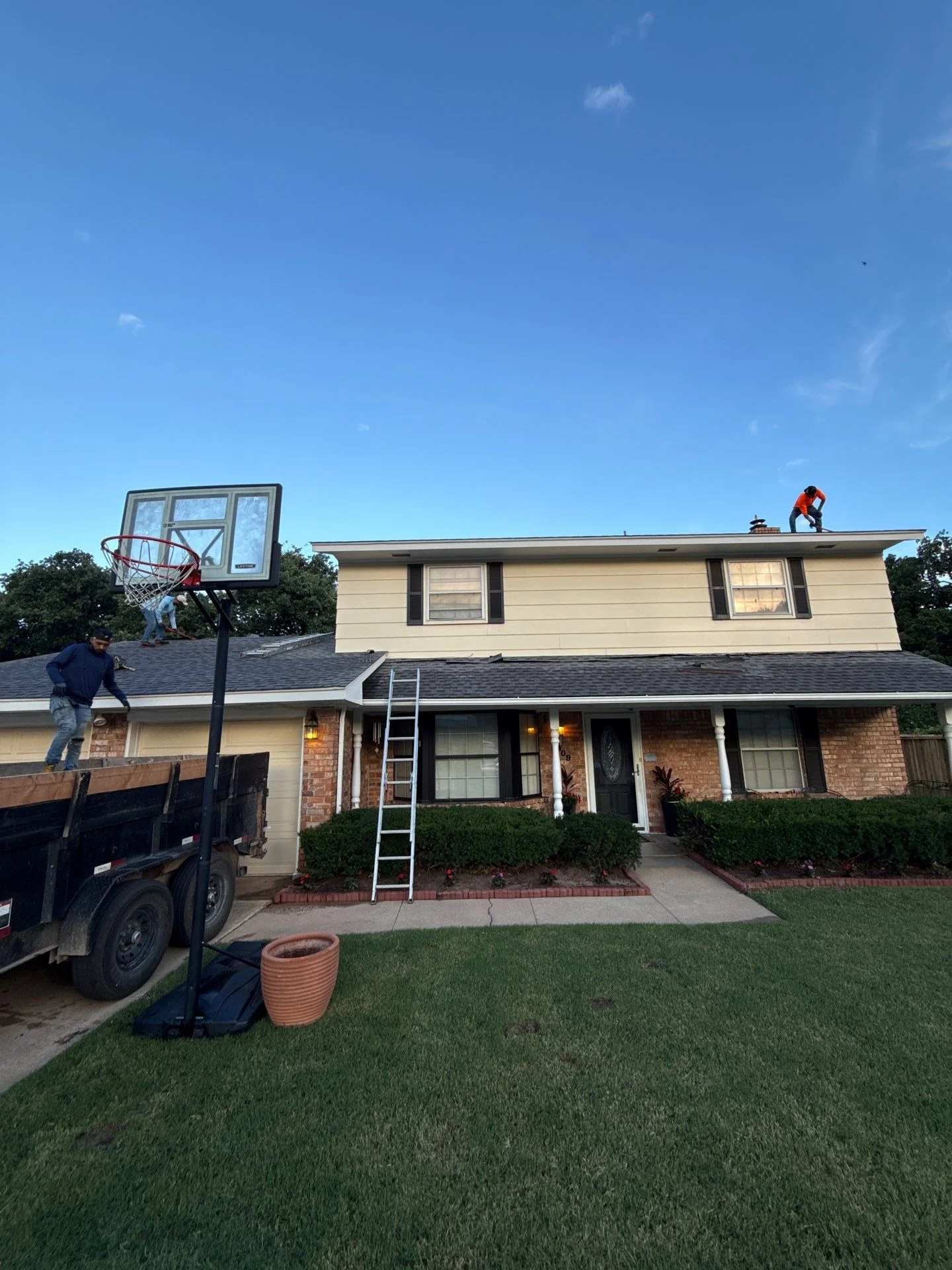 Two-story home with new asphalt shingle roof installation in progress, worker on roof with ladder staging