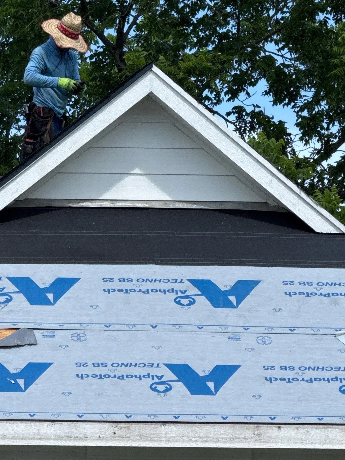 Roofer installing black shingles and white gable trim on residential roof peak