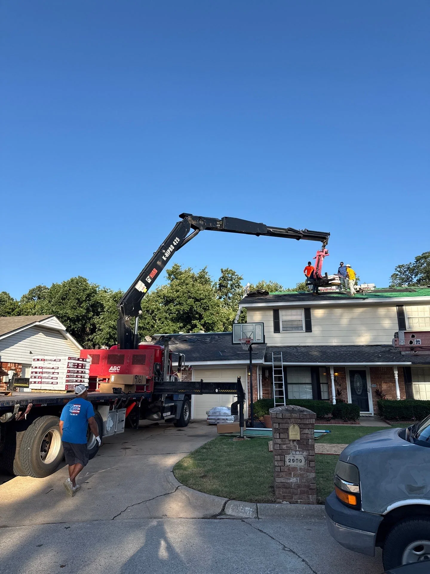 Crane lifting roofing materials and workers onto residential home roof during replacement project