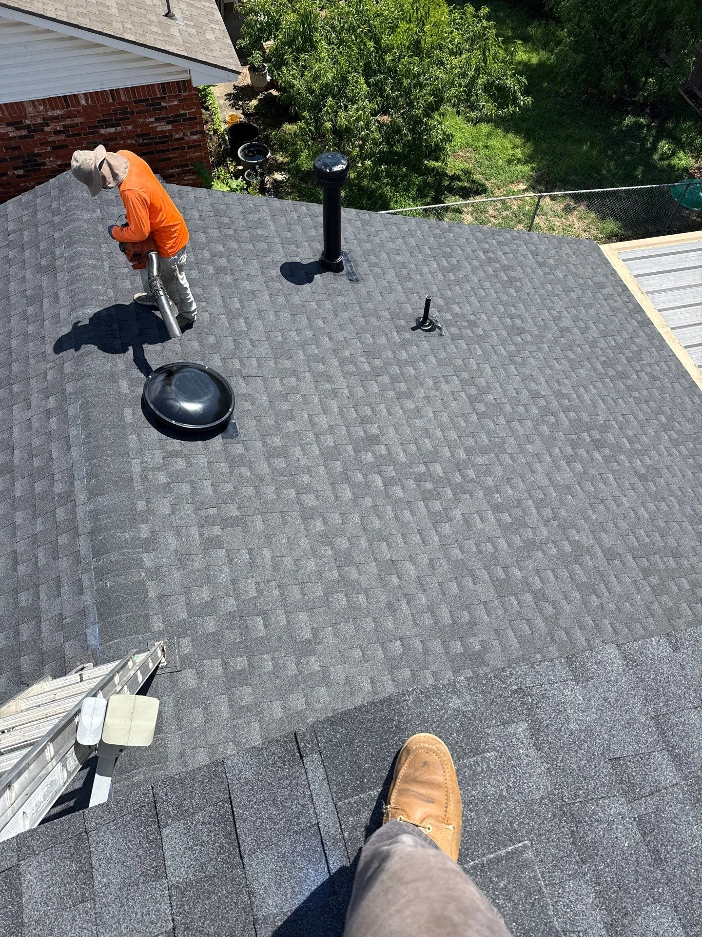 Roofer installing gray architectural shingles with proper vent flashing and penetration sealing