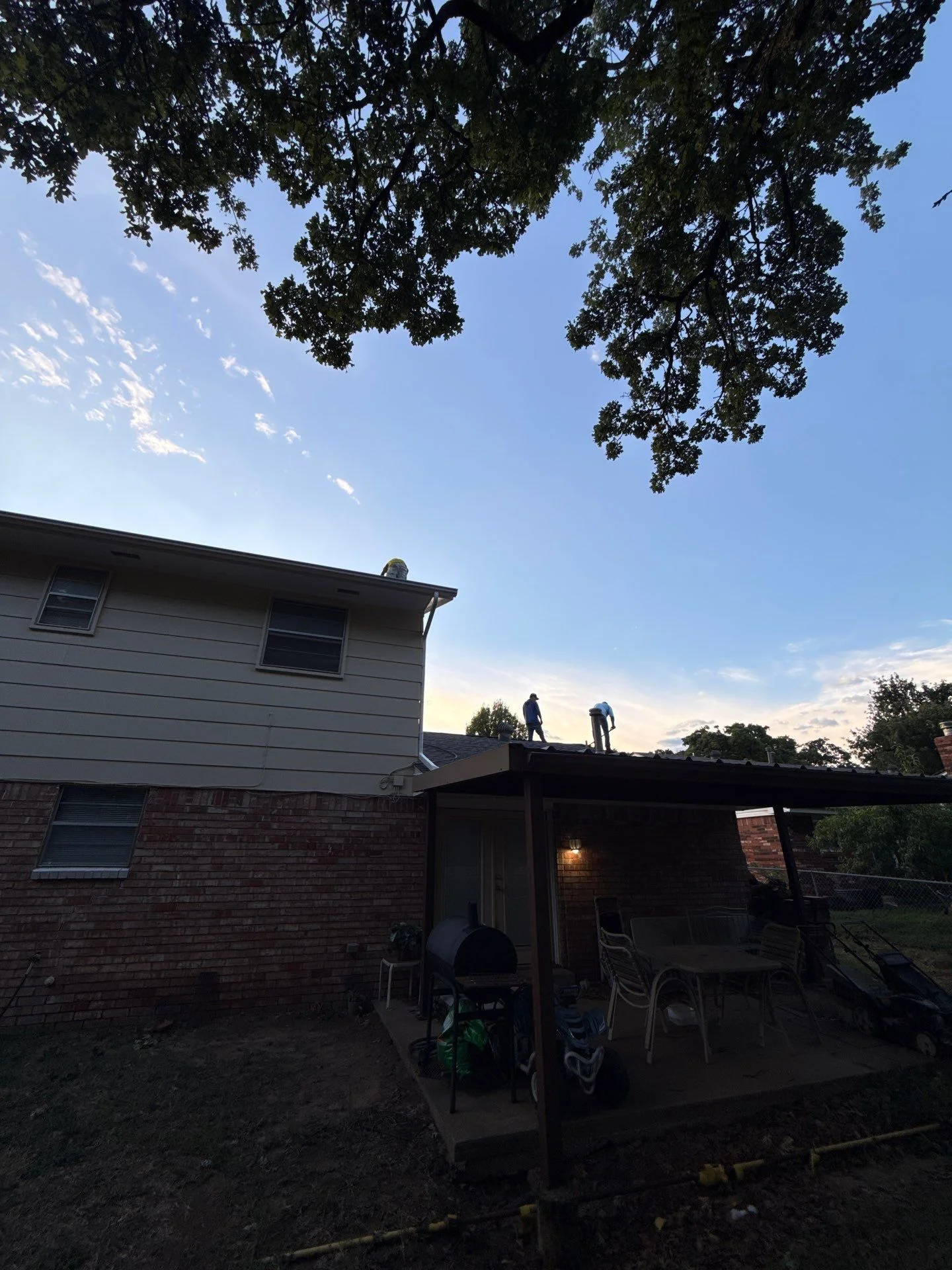Roofers installing new shingles on residential home roof with brick and siding exterior