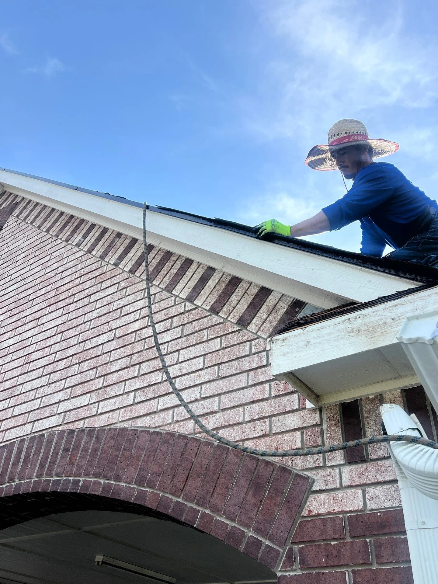 Worker installing seamless gutters on brick home with pitched roof and white fascia