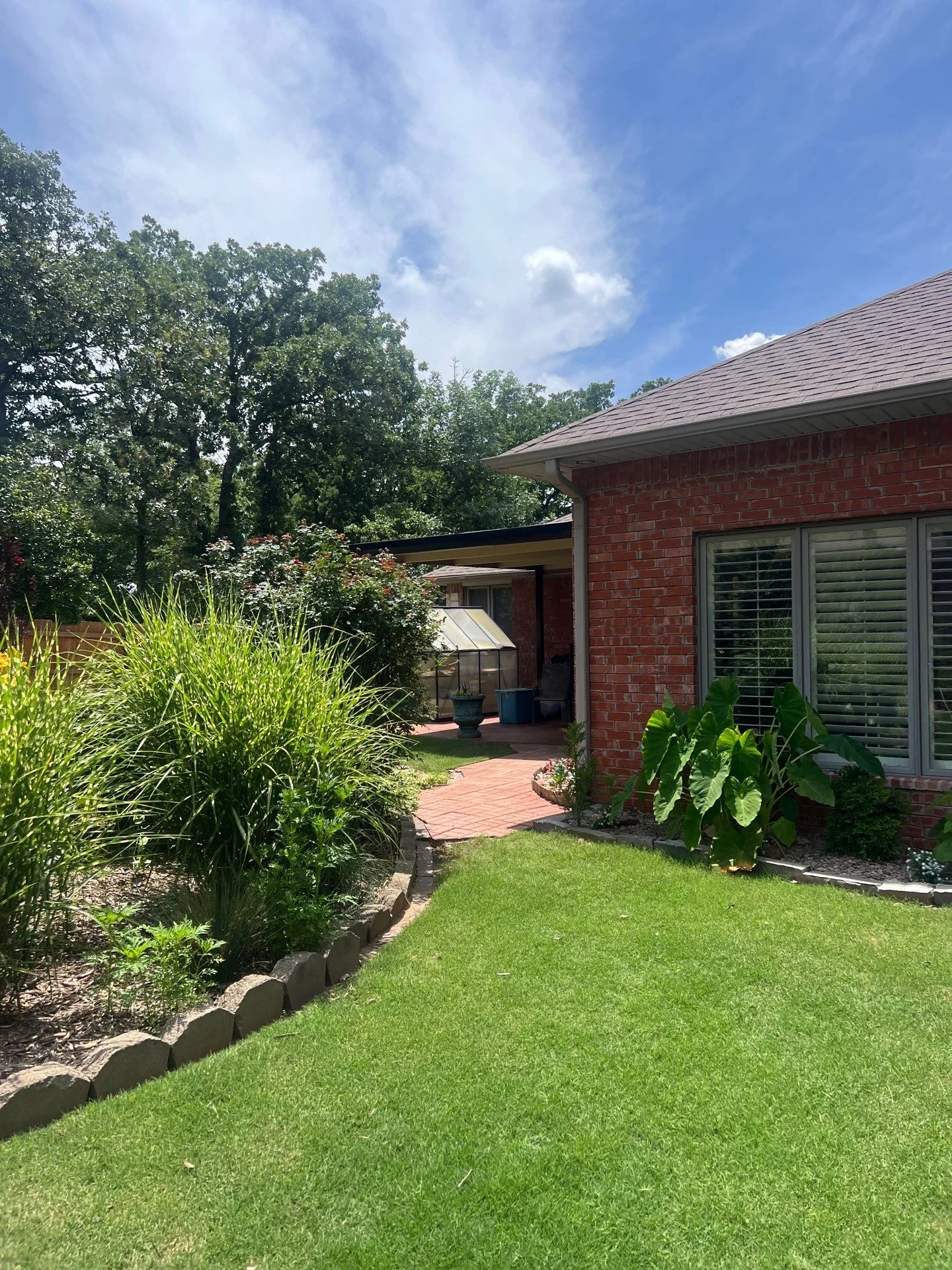 New architectural shingle roof on red brick home with patio overhang and landscaped yard