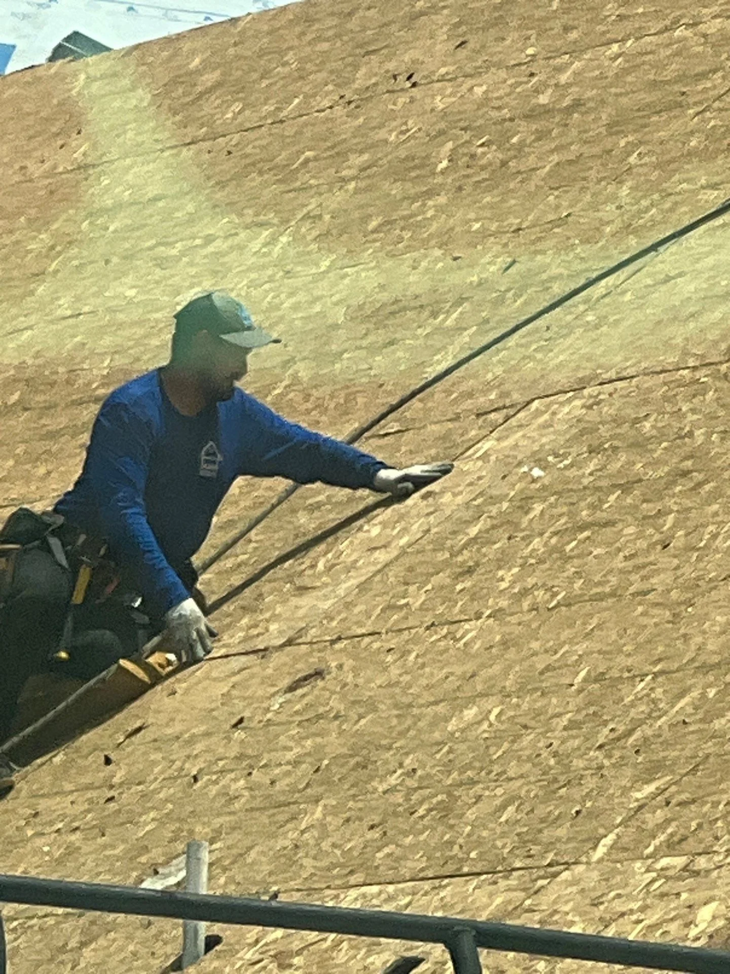 Roofer installing underlayment on steep-pitched OSB roof with pneumatic nailer